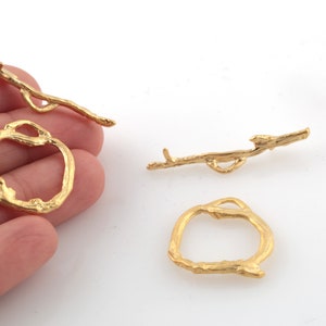 May include: Three gold-colored metal charms shaped like branches. Two charms are simple branches, and one charm is a circle made of intertwined branches.