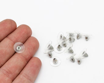 May include: A close-up of a group of clear plastic earring backs with silver metal posts. The earring backs are scattered on a white surface.