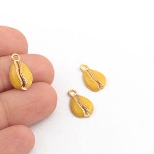 May include: Three gold-coloured metal charms shaped like seashells. The charms are yellow and have a gold-coloured outline. They are designed to be used for jewellery making.