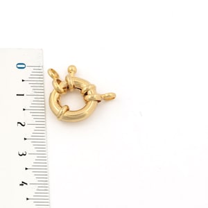 May include: Gold-toned metal clasp with a round ring and a decorative design. The clasp is approximately 1 inch in diameter.