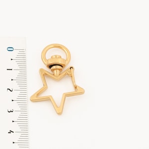 Puede incluir: Llavero de metal dorado en forma de estrella con cierre giratorio.