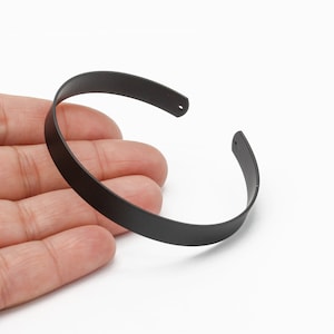 May include: A black metal bangle bracelet with a simple, rounded design.