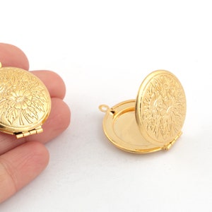 Op de afbeelding: Twee gouden metalen medaillon hangers met een bloemenmotief. De hangers zijn open en gesloten.