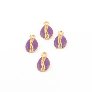 Könnte beinhalten: Vier goldfarbene Charms mit einer violetten Emaille-Oberfläche. Jeder Charm hat die Form einer halb geöffneten Muschel mit einer goldfarbenen Linie in der Mitte.