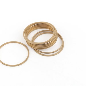 Peut inclure: Un ensemble de dix bracelets en métal de couleur or empilés les uns sur les autres. Un bracelet est séparé de la pile et est couché sur le côté.