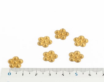 Puede incluir: Seis adornos metálicos de color dorado en forma de flor con puntas puntiagudas, cada uno con nueve puntos, dispuestos sobre una superficie blanca con una regla para la escala.