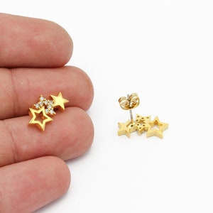 May include: Gold tone star shaped earrings with clear cubic zirconia stones. The earrings are stacked on top of each other.