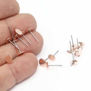 May include: A close-up of rose gold earring posts with flat round tops. The posts are made of metal and are designed for use with jewelry making.