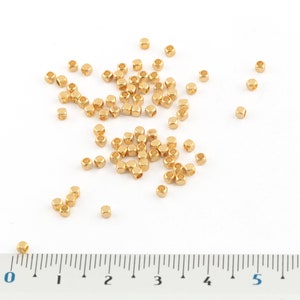 May include: A close-up of a ruler measuring 7 inches with a scattering of small, gold-colored, square-shaped beads.