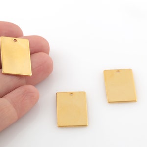 Puede incluir: Tres etiquetas rectangulares de metal de color dorado con un agujero en la parte superior. Las etiquetas están en blanco y listas para ser personalizadas.