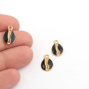 May include: Three gold-colored metal charms with black enamel. Each charm is shaped like a teardrop with a gold-colored design.