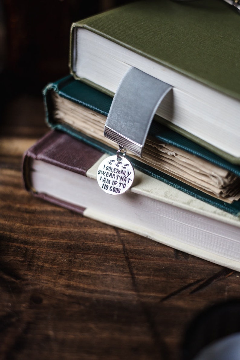 May include: A stack of three books with a silver bookmark charm that reads "I solemnly swear that I am up to no good".