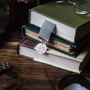 May include: A stack of three books with a silver bookmark charm that reads "I solemnly swear that I am up to no good".