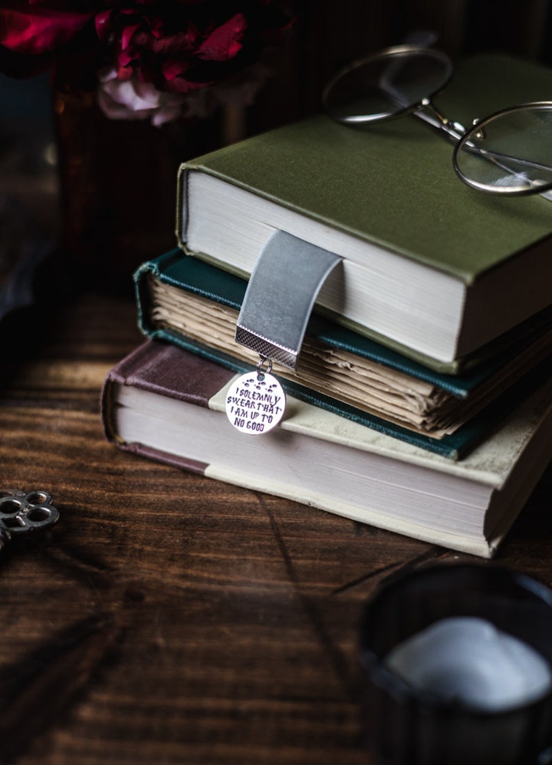 May include: A stack of three books with a silver bookmark charm that reads "I solemnly swear that I am up to no good".