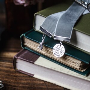 May include: A stack of three books with a grey velvet ribbon bookmark. The bookmark has two charms, one is a small figure and the other is a round charm with the text "I solemnly swear that I am up to no good".
