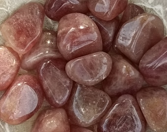Può includere: Una collezione di pietre di quarzo rosa levigate in una ciotola. Le pietre sono di colore rosa chiaro e hanno una finitura liscia e lucida.