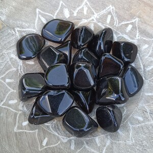 Peut inclure: Une collection de pierres d'obsidienne noire roulées. Les pierres sont lisses et polies, avec une finition brillante.