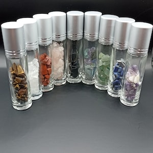 Op de afbeelding: Tien kleine glazen flesjes met zilveren dopjes, elk gevuld met verschillende gekleurde kristallen. De flesjes zijn in een halve cirkel op een zwart oppervlak gerangschikt.