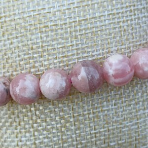 Puede incluir: Un brazalete de piedras preciosas rosa y blanco con cuentas redondas. El brazalete está hecho de piedras naturales y es un hermoso accesorio para cualquier ocasión.