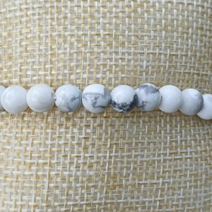 May include: White howlite beaded bracelet with grey veining. The bracelet is made of round beads and is approximately 7 inches in length.