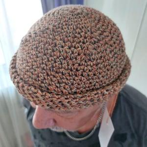 May include: A crocheted hat with a brown, orange, and white color pattern. The hat has a rounded crown and a brim.