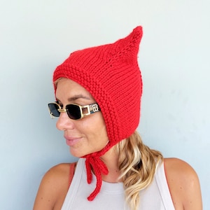May include: A red knitted hat with a pointed top and ear flaps. The hat has a tie that can be tied under the chin.