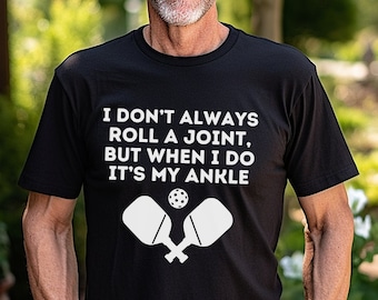 May include: Black t-shirt with white text that reads "I don't always roll a joint, but when I do it's my ankle."  The text is accompanied by a white image of two crossed pickleball paddles and a pickleball.