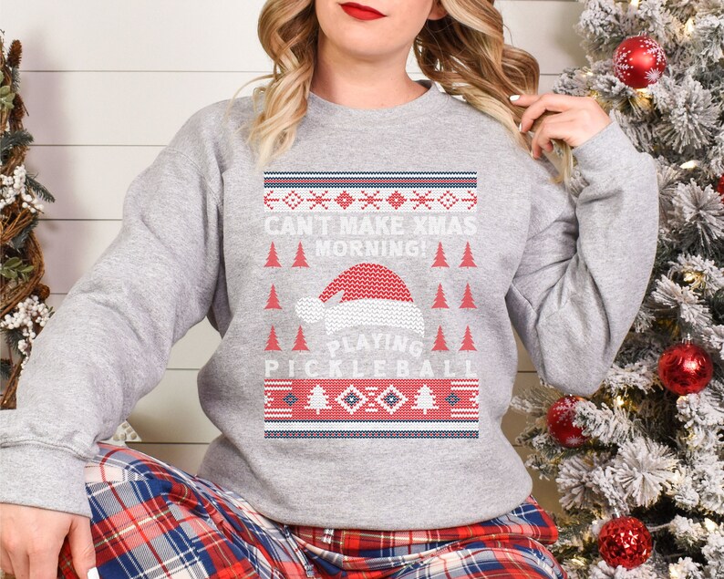 May include: Gray Christmas sweater with a red and white Santa hat and the text "Can't Make Xmas Morning! Playing Pickleball".