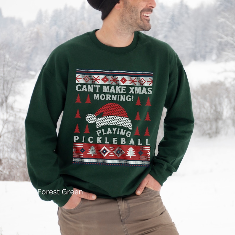May include: Forest green Christmas sweater with a red and white pattern. The sweater has the text "Can't make Xmas morning! Playing Pickleball" on it.