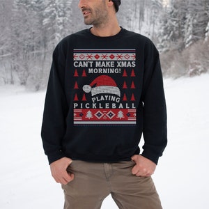 May include: A navy blue Christmas sweater with a red and white knit pattern. The sweater features a Santa hat and the text "Can't Make Xmas Morning! Playing Pickleball".