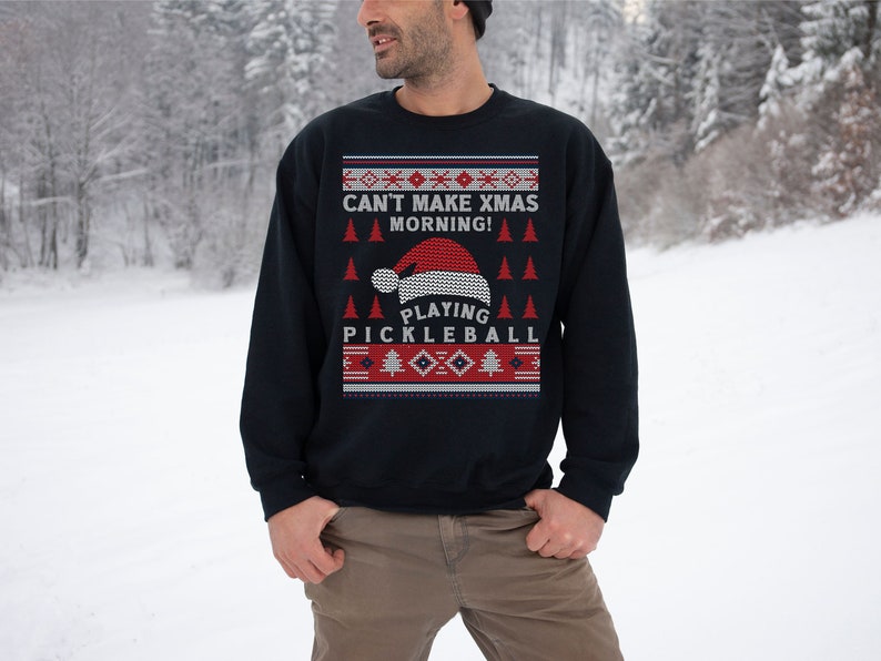 May include: A navy blue Christmas sweater with a red and white knit pattern. The sweater features a Santa hat and the text "Can't Make Xmas Morning! Playing Pickleball".