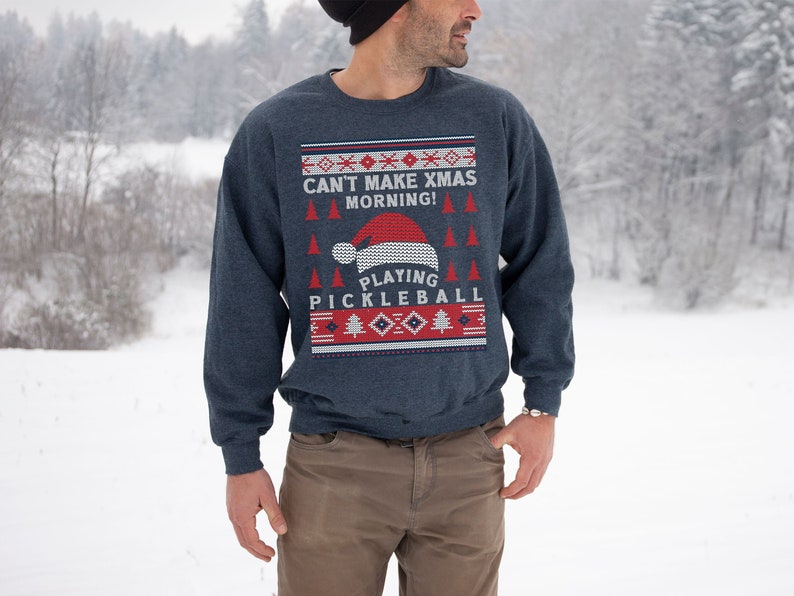 May include: A blue Christmas sweater with a red and white knit pattern. The sweater features the text "Can't Make Xmas Morning! Playing Pickleball".