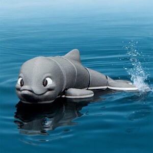 Puede incluir: Un juguete de delfín gris con ojos blancos y boca negra, flotando en agua azul.