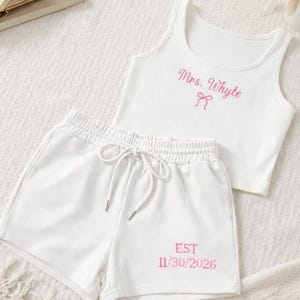 May include: White ribbed tank top and shorts set. The tank top features the text "Mrs. Whyte" in pink script with a bow. The shorts have the text "EST 11/30/2026" in pink. The shorts have a drawstring waist.
