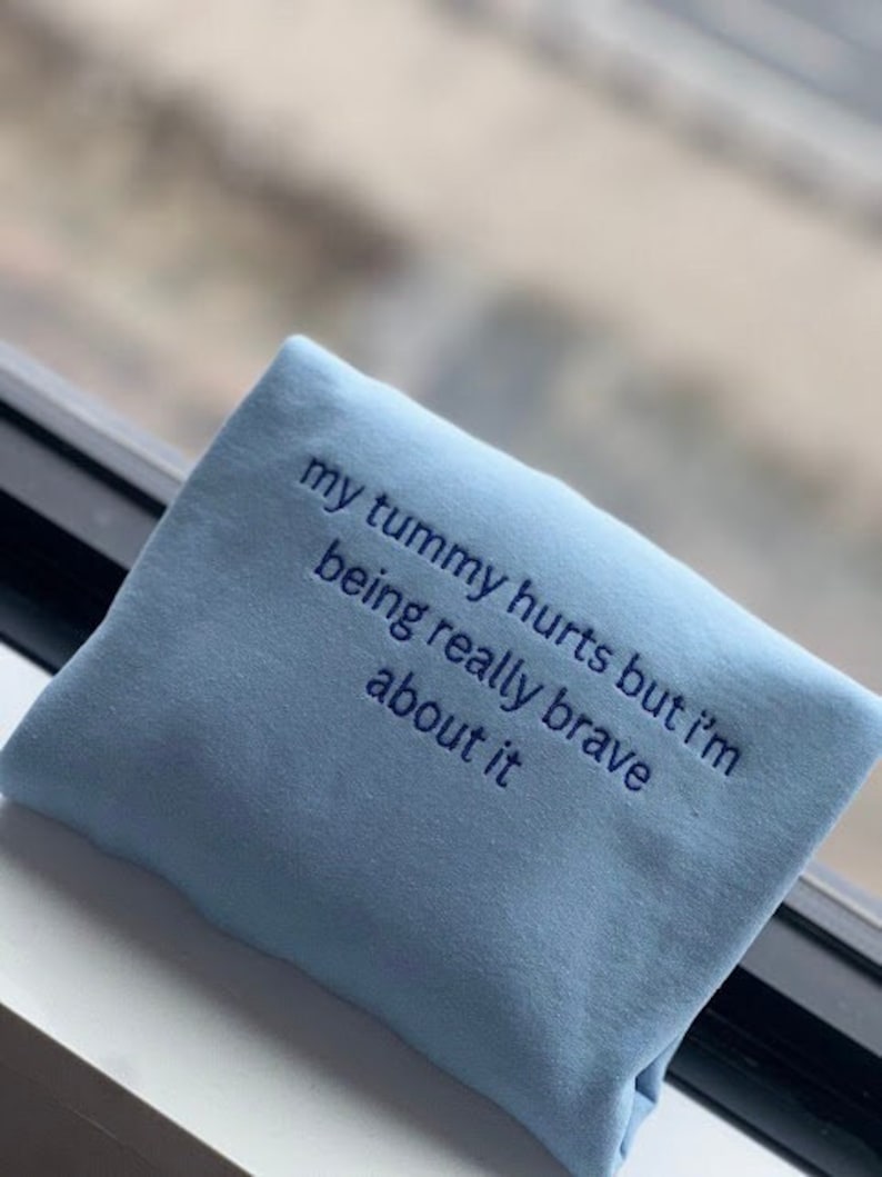 May include: Light blue sweatshirt with the text "my tummy hurts but i'm being really brave about it" embroidered in blue.