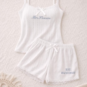 Könnte beinhalten: Weißes Pyjama-Set mit einem Camisole-Top und Shorts. Das Top hat dünne Träger, eine Schleife und den gestickten Text "Mrs. Flowers". Die Shorts haben eine Schleife und den gestickten Text "EST. 03/17/2027".
