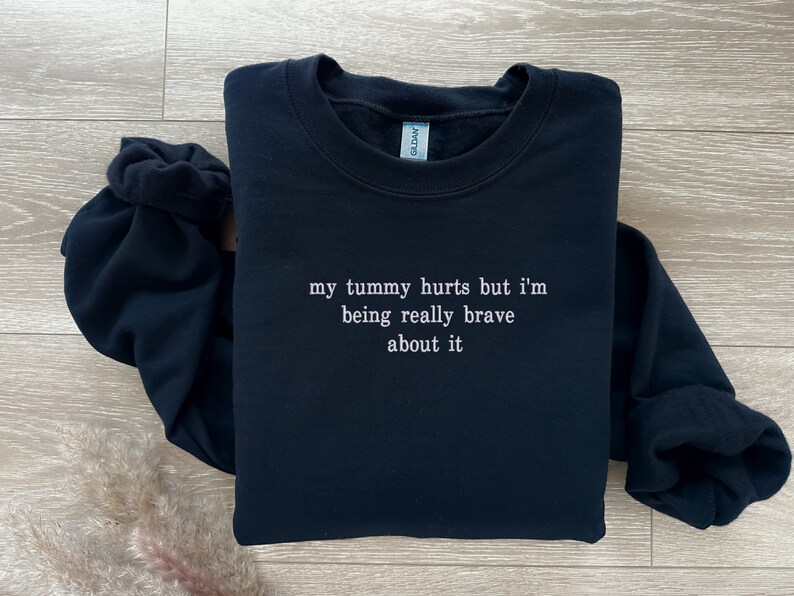 May include: Black sweatshirt with the text "my tummy hurts but i'm being really brave about it" in white.