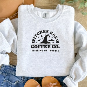 May include: Grey sweatshirt with a black graphic design that says "Witches Brew Coffee Co. Stirring Up Trouble" with a witch's hat and stars.