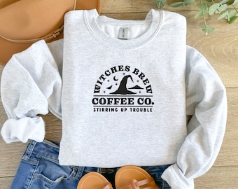 Puede incluir: Sudadera gris con un diseño gráfico negro que dice "Witches Brew Coffee Co. Stirring Up Trouble" con un sombrero de bruja y estrellas.
