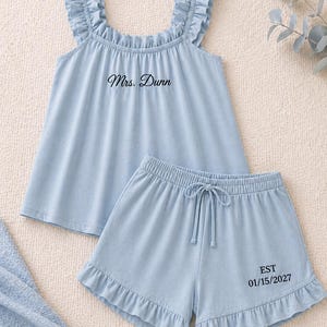 May include: Light blue pajama set with a ruffled top and shorts. The top has the text "Mrs. Dunn" printed on it. The shorts have a drawstring waist and the text "EST 01/15/2027".