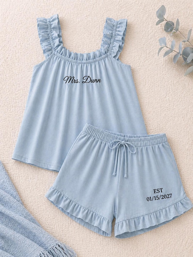 May include: Light blue pajama set with a ruffled top and shorts. The top has the text "Mrs. Dunn" printed on it. The shorts have a drawstring waist and the text "EST 01/15/2027".