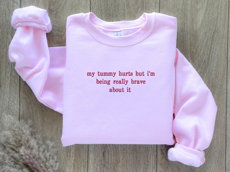 May include: Pink sweatshirt with the text "my tummy hurts but i'm being really brave about it" in red.