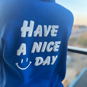May include: A royal blue sweatshirt with the text "Have a Nice Day" in white with a white smiley face.