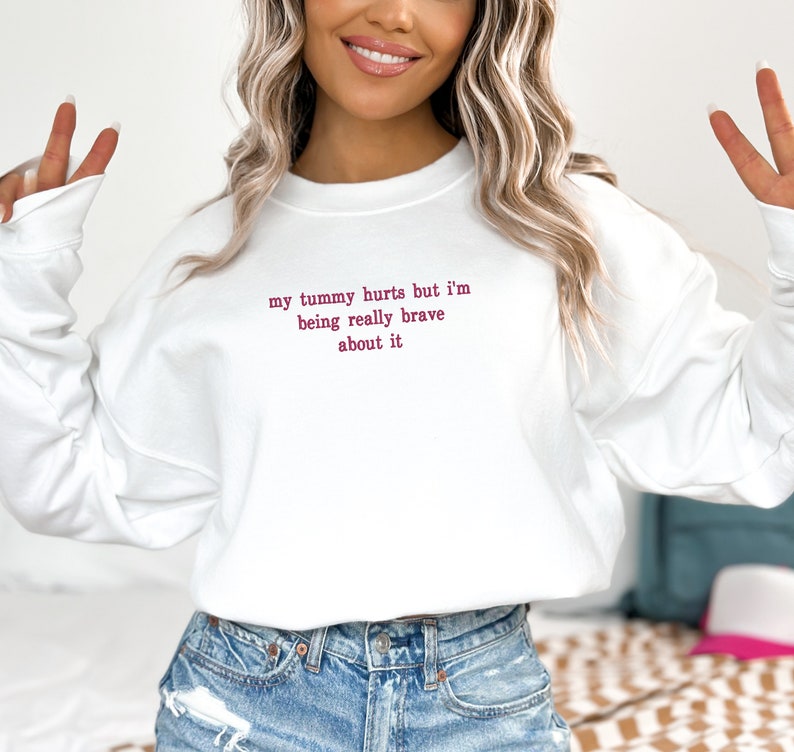 May include: White sweatshirt with the text "my tummy hurts but I'm being really brave about it" in pink.