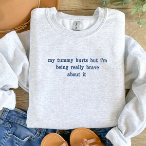 May include: Gray sweatshirt with the text "my tummy hurts but i'm being really brave about it" in blue.