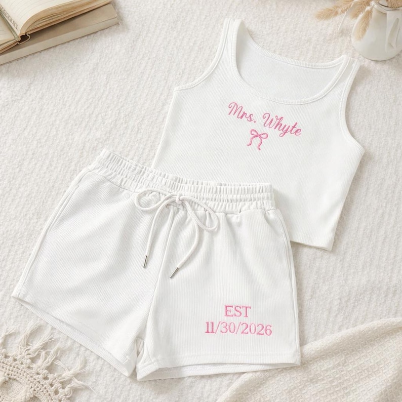 May include: White ribbed tank top and matching shorts set. The tank top has the text "Mrs. Whyte" in pink script with a bow. The shorts have the text "EST 11/30/2026" in pink. The shorts have a drawstring waist.