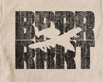 May include: A beige t-shirt with a black graphic print of an airplane silhouette with the text "BEBER" and "REAKT" in a distressed font.