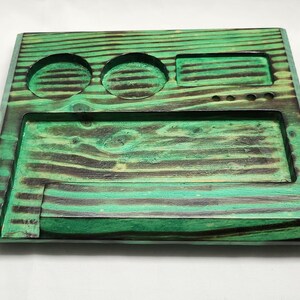 May include: A green wooden tray with three circular indentations and a rectangular indentation. The tray has a dark wood grain pattern.