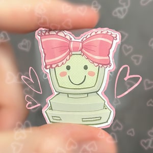 May include: A sticker featuring a vintage computer with a smiling face and a pink bow. The computer is light green with a pink outline, and the bow has white stripes. Pink hearts are in the background.