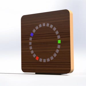 May include: A square wooden device with a dark brown wood grain finish. The device has a circular display of small, illuminated squares. The display shows a blue, green, and red square. The edges of the device are a lighter wood colour.